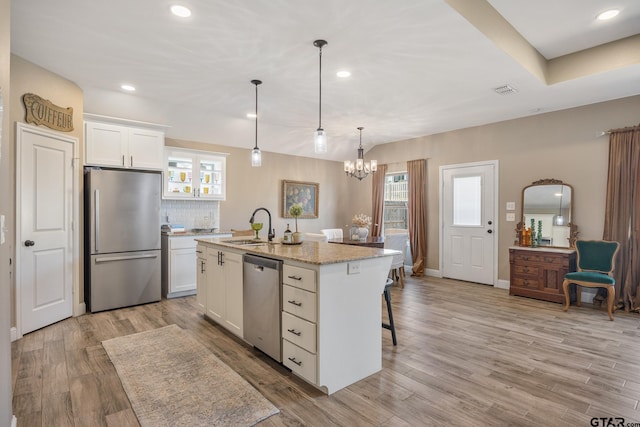 kitchen featuring stainless steel appliances, hanging light fixtures, a kitchen island with sink, light hardwood / wood-style flooring, and white cabinets