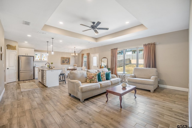 living room with a wealth of natural light, a raised ceiling, and light hardwood / wood-style floors