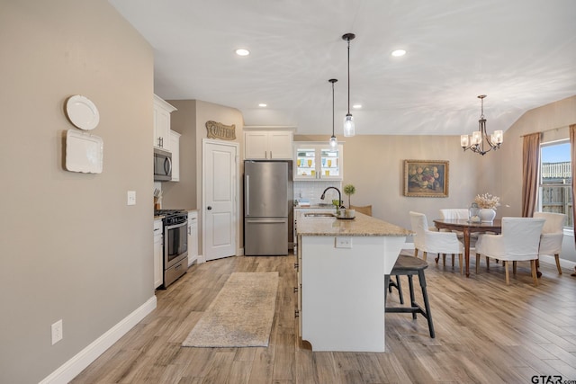 kitchen featuring stainless steel appliances, light hardwood / wood-style floors, white cabinetry, an island with sink, and pendant lighting