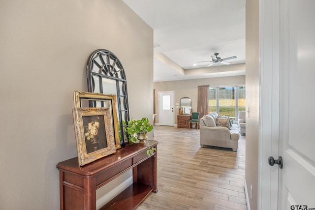 hall with light hardwood / wood-style floors and a raised ceiling