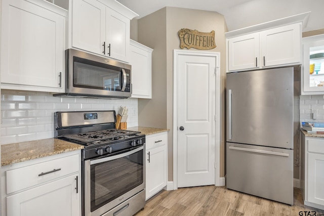 kitchen with white cabinets, appliances with stainless steel finishes, light hardwood / wood-style floors, and light stone countertops