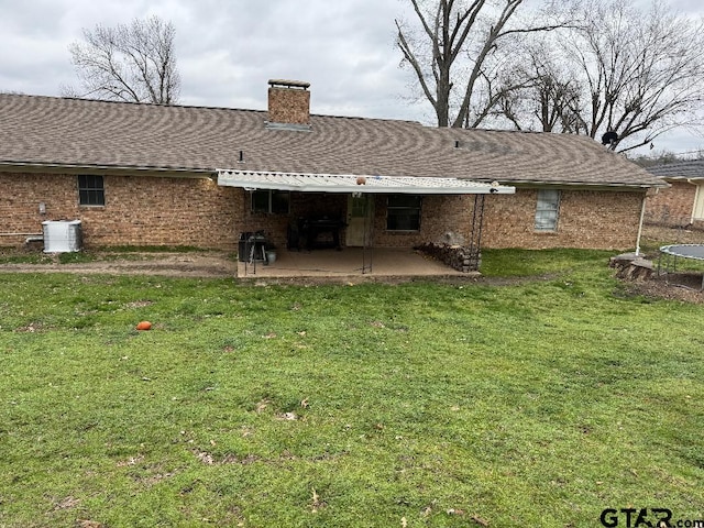 back of property with a shingled roof, brick siding, a patio, and a lawn