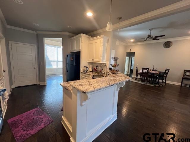 kitchen featuring black refrigerator, a breakfast bar, sink, decorative light fixtures, and white cabinetry