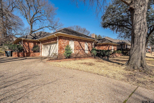 view of front of property featuring a garage, driveway, brick siding, and a chimney