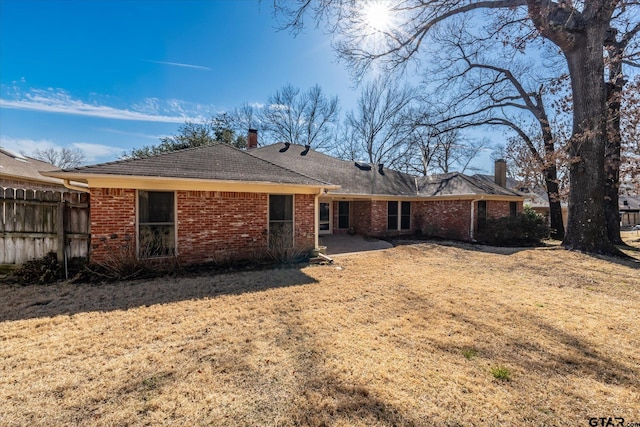 back of house with a yard, brick siding, a chimney, and fence