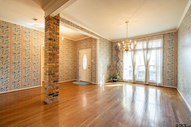 unfurnished room with a notable chandelier, ornamental molding, hardwood / wood-style flooring, and wallpapered walls