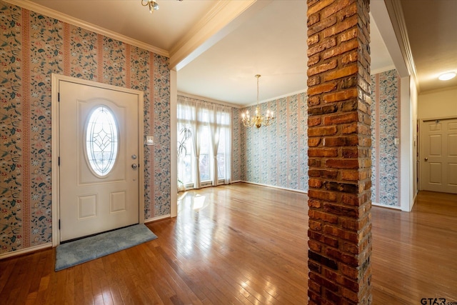 foyer with wallpapered walls, ornamental molding, a chandelier, baseboards, and hardwood / wood-style flooring