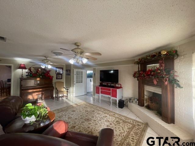 living room featuring ceiling fan, light tile patterned floors, a textured ceiling, and a brick fireplace