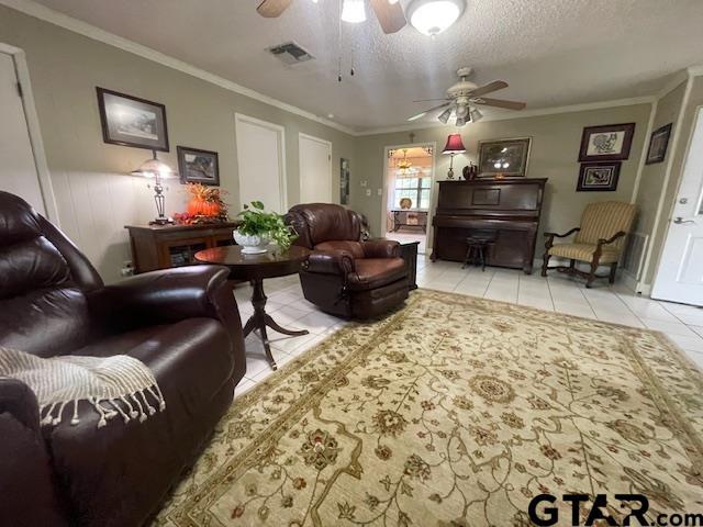 tiled living room with ceiling fan, a textured ceiling, and ornamental molding