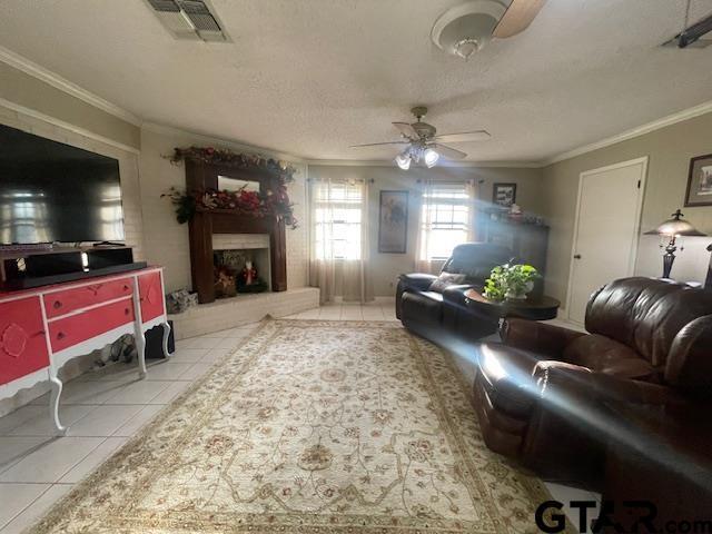 living room with a textured ceiling, ceiling fan, light tile patterned floors, and crown molding