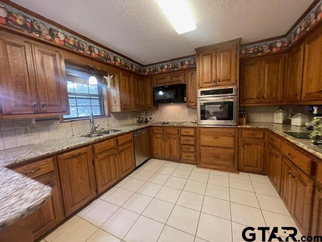 kitchen with sink, a textured ceiling, tasteful backsplash, light stone counters, and stainless steel appliances