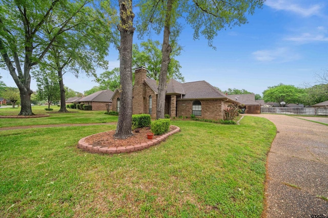 view of front facade with a front yard, a shingled roof, fence, concrete driveway, and brick siding