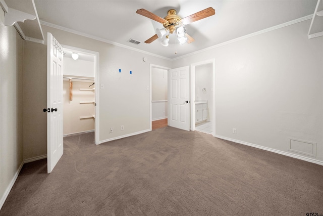 unfurnished bedroom featuring baseboards, a spacious closet, carpet flooring, crown molding, and visible vents