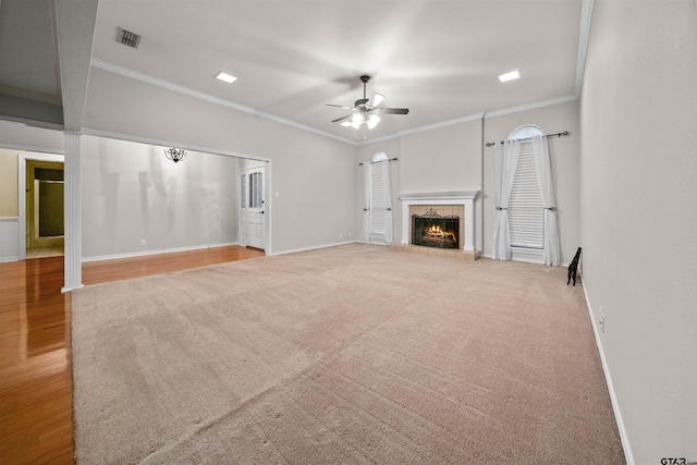unfurnished living room featuring baseboards, a warm lit fireplace, ornamental molding, a ceiling fan, and carpet floors
