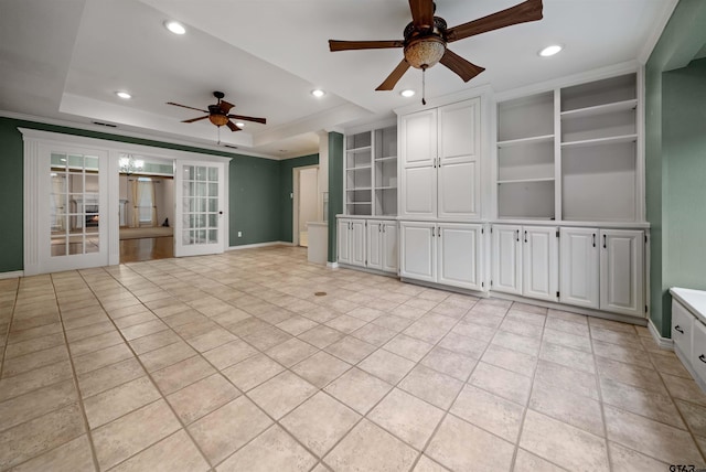 empty room featuring french doors, a tray ceiling, built in features, and a ceiling fan