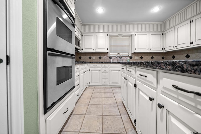 kitchen with light tile patterned floors, white cabinetry, backsplash, appliances with stainless steel finishes, and a sink