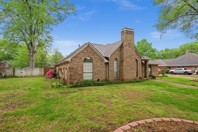 view of front facade featuring a front yard, a chimney, fence, brick siding, and roof with shingles