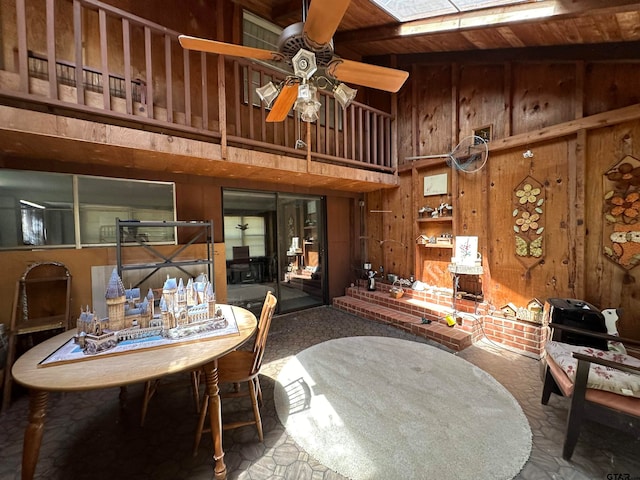 dining area with wood walls, wooden ceiling, ceiling fan, a skylight, and a high ceiling