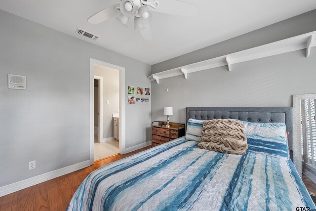 bedroom with wood finished floors, visible vents, connected bathroom, baseboards, and ceiling fan