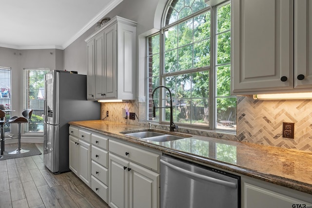 kitchen with stainless steel appliances, a sink, ornamental molding, and tasteful backsplash