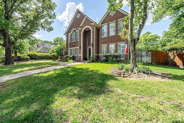 traditional-style house featuring brick siding, a front yard, and fence