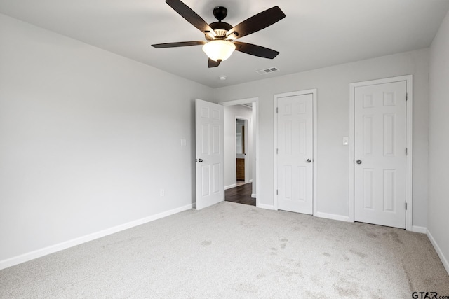 unfurnished bedroom featuring ceiling fan, dark carpet, visible vents, and baseboards