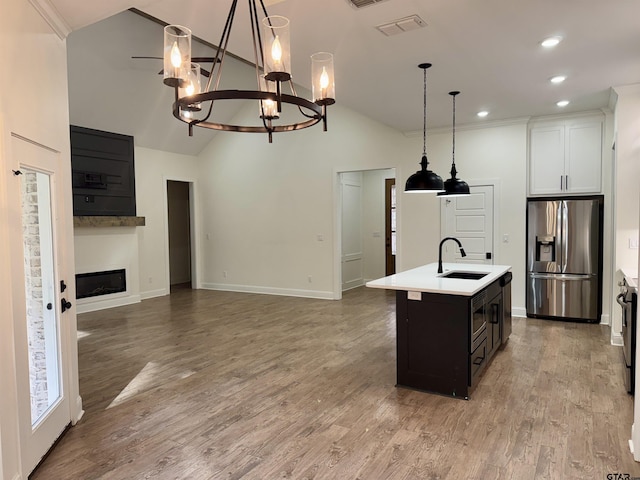 kitchen with sink, hanging light fixtures, stainless steel fridge with ice dispenser, a kitchen island with sink, and white cabinets