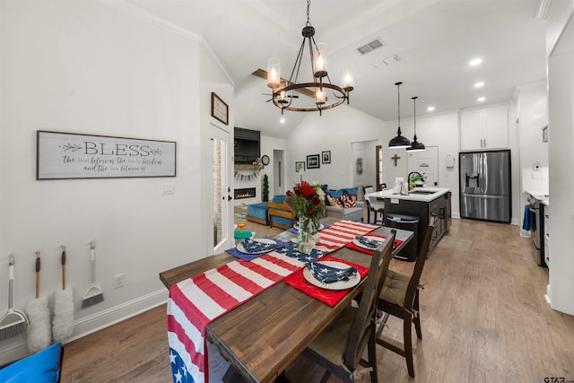 dining room with sink, hardwood / wood-style flooring, a fireplace, a chandelier, and lofted ceiling