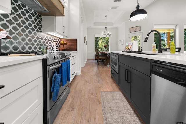 kitchen with white cabinets, appliances with stainless steel finishes, an inviting chandelier, and pendant lighting