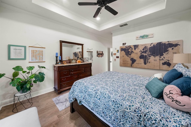 bedroom featuring ceiling fan, wood-type flooring, ornamental molding, and a tray ceiling