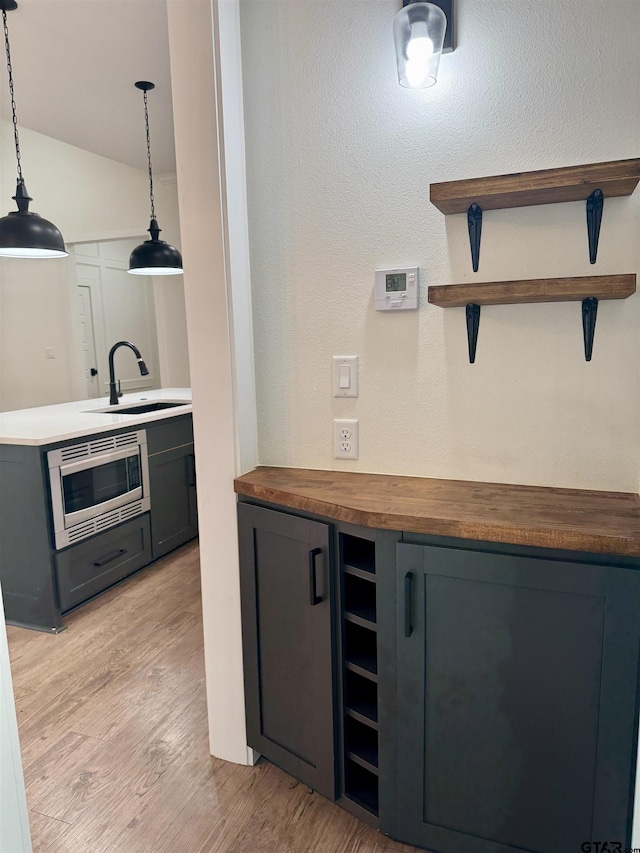 bar with sink, stainless steel microwave, wood counters, pendant lighting, and light wood-type flooring