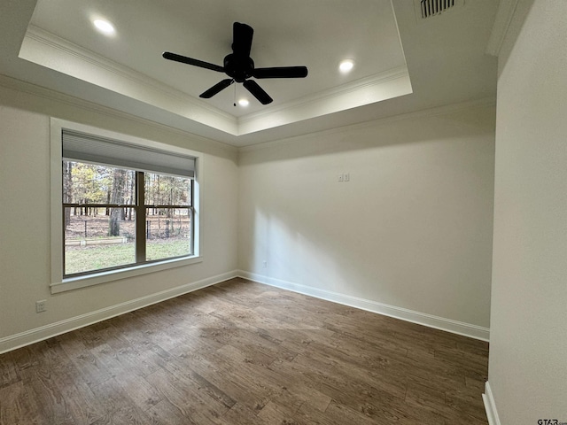 empty room with a tray ceiling, ceiling fan, dark wood-type flooring, and ornamental molding