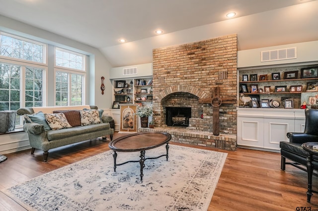 living room featuring vaulted ceiling, a fireplace, and light hardwood / wood-style floors