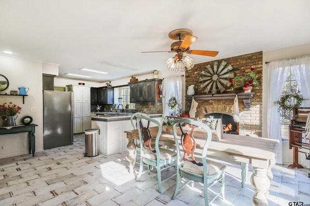 dining space featuring a brick fireplace, sink, ceiling fan, and brick wall