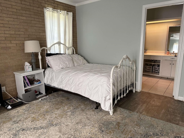 bedroom featuring brick wall, light wood-type flooring, crown molding, and connected bathroom