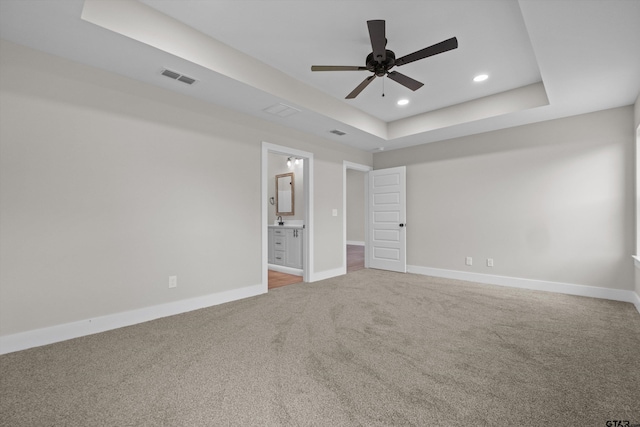 unfurnished bedroom with ceiling fan, carpet, ensuite bathroom, and a raised ceiling