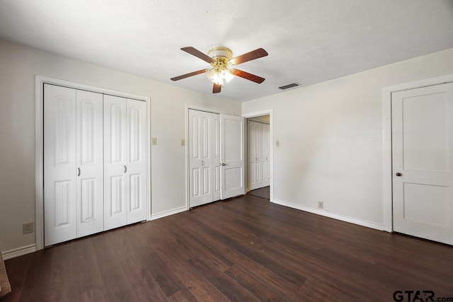 unfurnished bedroom featuring ceiling fan, a textured ceiling, dark wood-type flooring, and multiple closets