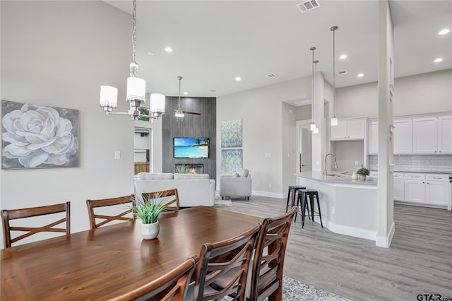 dining space with ceiling fan, a large fireplace, a high ceiling, and light wood-type flooring