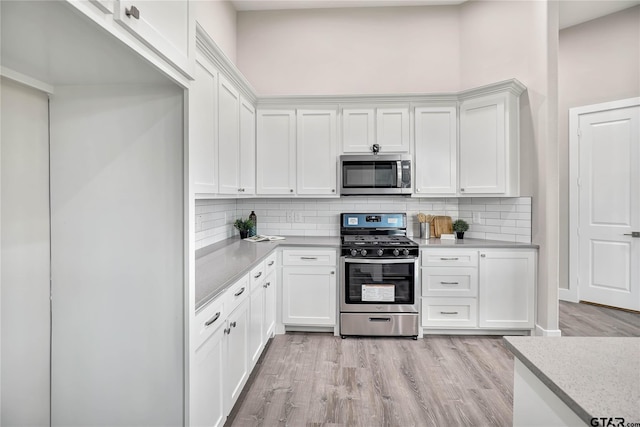 kitchen with a high ceiling, white cabinets, decorative backsplash, appliances with stainless steel finishes, and light hardwood / wood-style floors