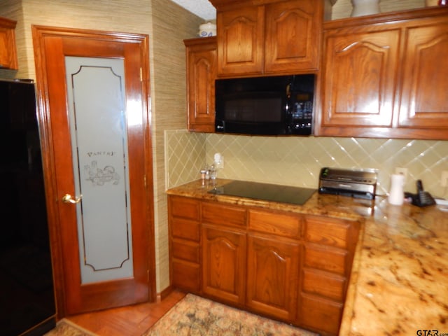 kitchen with light stone countertops, backsplash, and black appliances