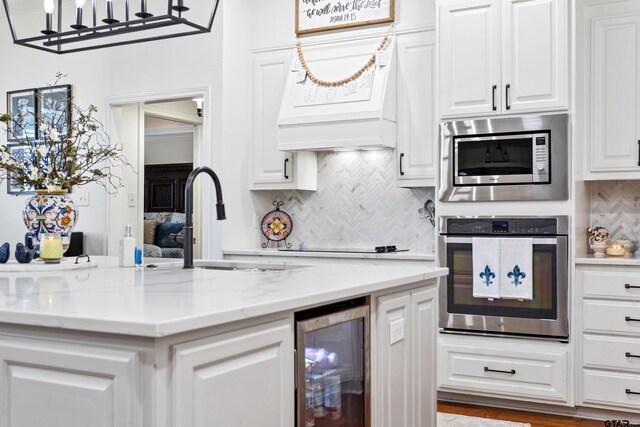 16050 Stonebriar Ct, Lindale, TX 75771 - kitchen featuring appliances with stainless steel finishes, beverage cooler, white cabinetry, backsplash, and light stone countertops