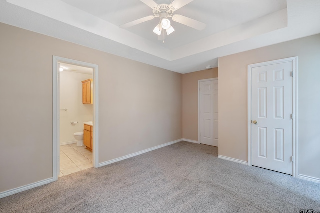 unfurnished bedroom featuring a raised ceiling, light carpet, ceiling fan, and ensuite bath