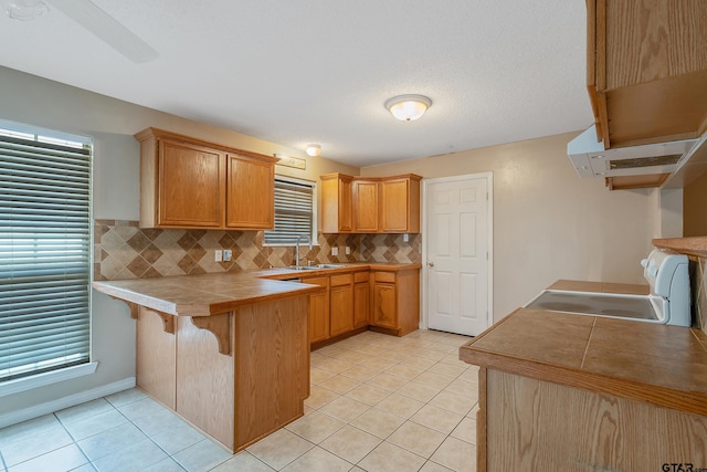 kitchen featuring sink, kitchen peninsula, light tile patterned floors, range, and decorative backsplash