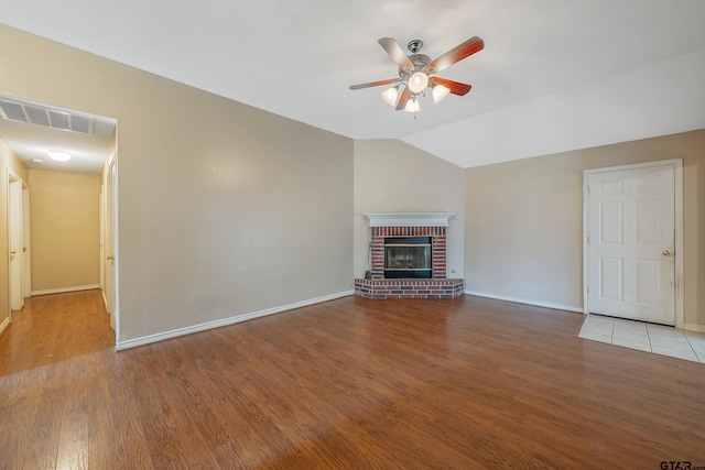 unfurnished living room featuring light wood-type flooring, lofted ceiling, ceiling fan, and a brick fireplace