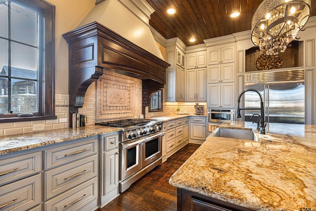 kitchen with premium appliances, decorative backsplash, sink, hanging light fixtures, and light stone counters