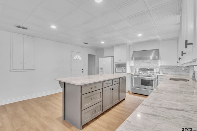 kitchen with light wood-type flooring, light stone counters, white appliances, wall chimney range hood, and sink