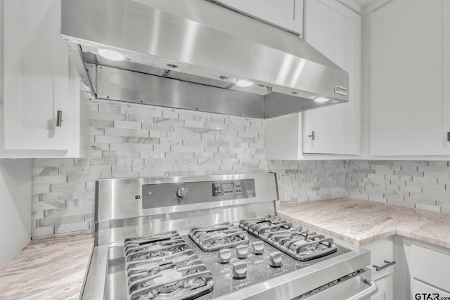 kitchen with white cabinets, stainless steel gas stove, light stone countertops, and backsplash