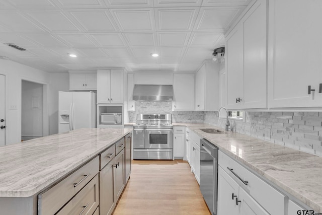 kitchen with light wood-type flooring, stainless steel appliances, wall chimney range hood, sink, and white cabinets