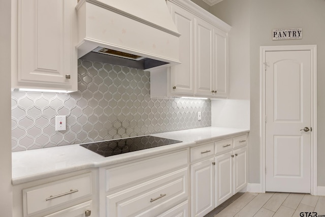 kitchen with black electric stovetop, decorative backsplash, white cabinetry, and premium range hood