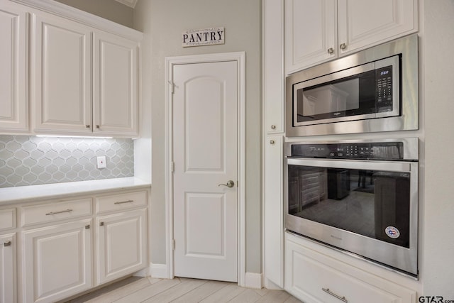 kitchen with white cabinets, light wood-type flooring, stainless steel appliances, and tasteful backsplash